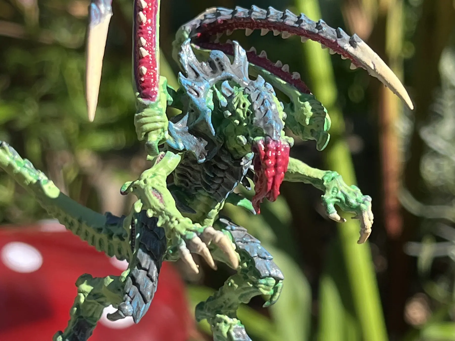 A highly detailed hand-painted green creature miniature photographed outdoors